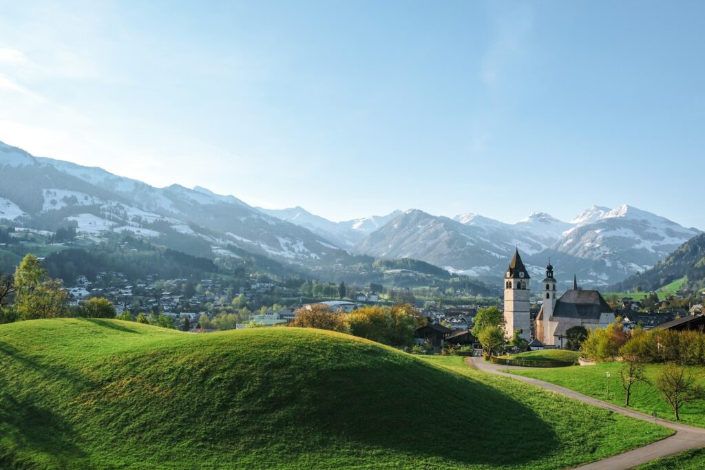 Traditional Austrian church in the middle of green fields with mountains in the backgroun